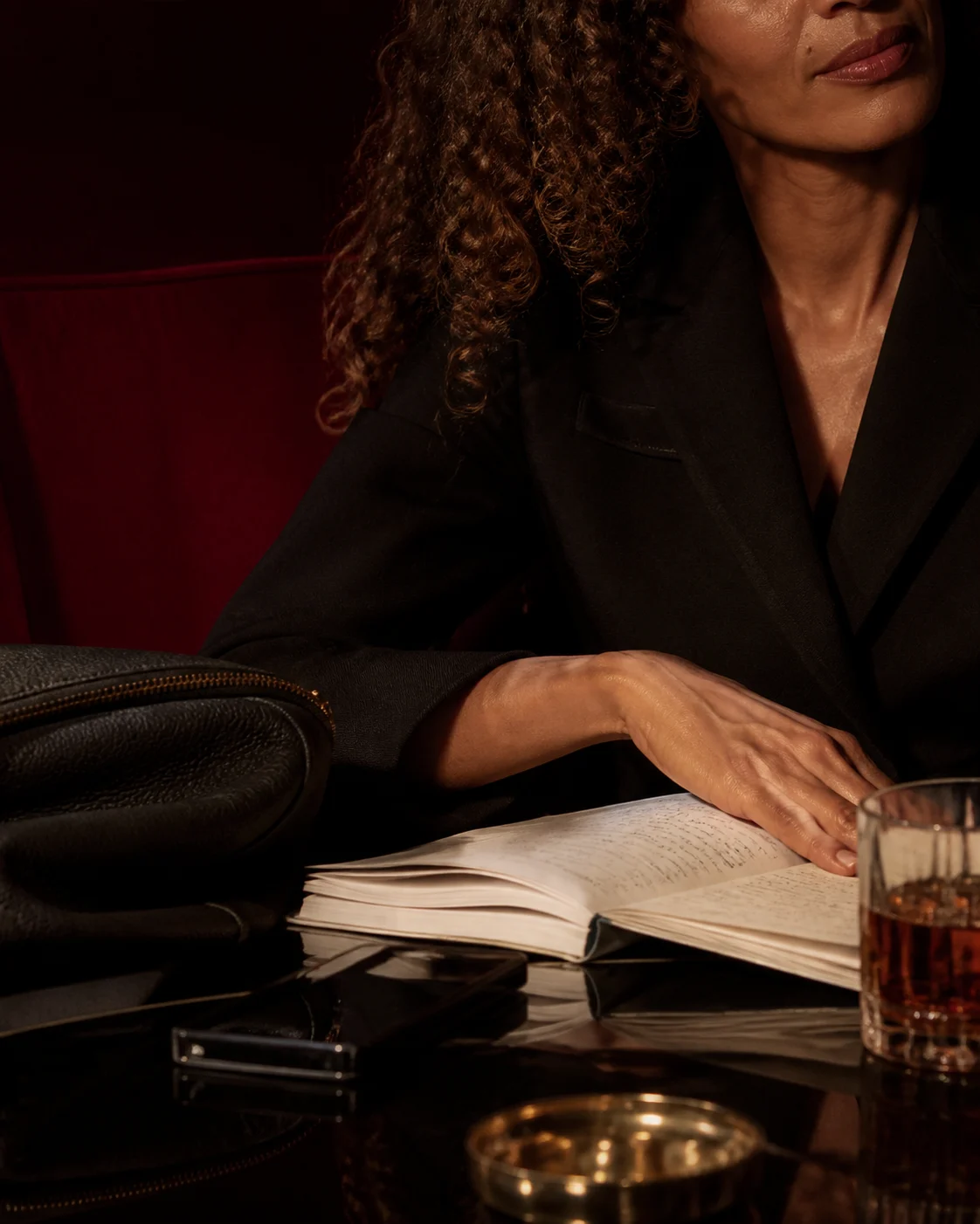 A woman in a dark blazer with an open notebook, a glass beside her, in low light