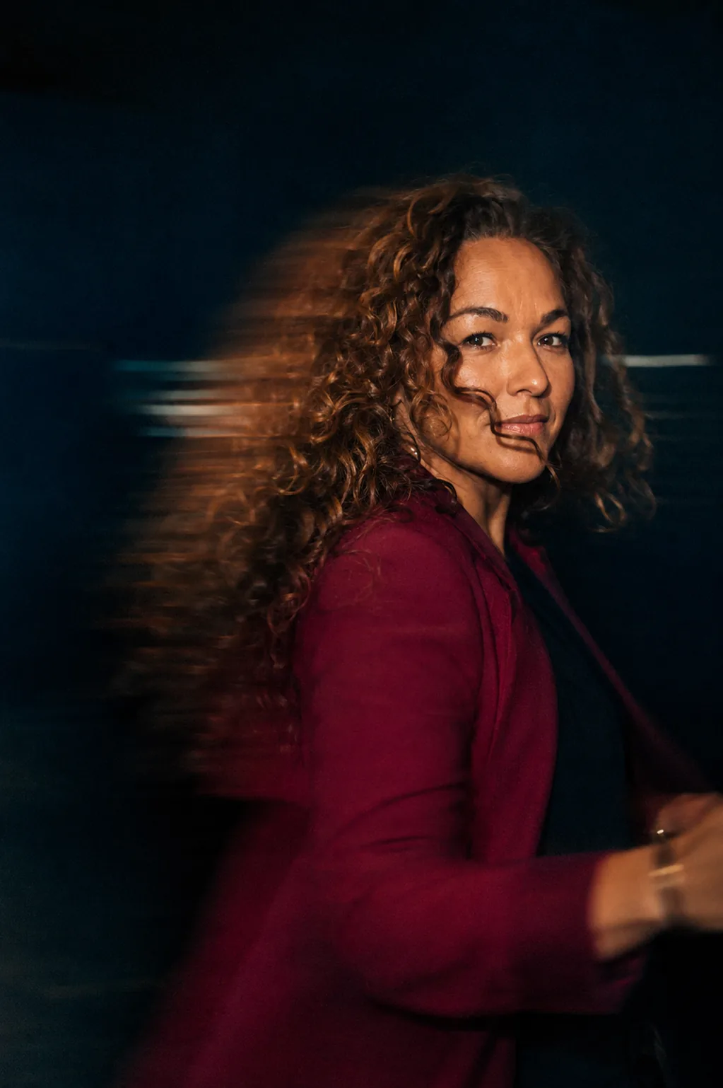 Maria-Inés in a burgundy blazer, turning toward the camera as the background streaks into motion